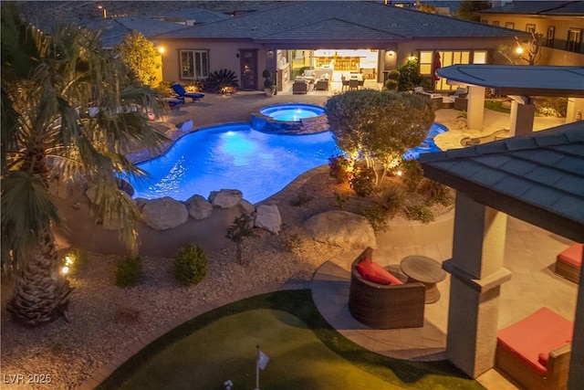 pool at night featuring a patio and a pool with connected hot tub