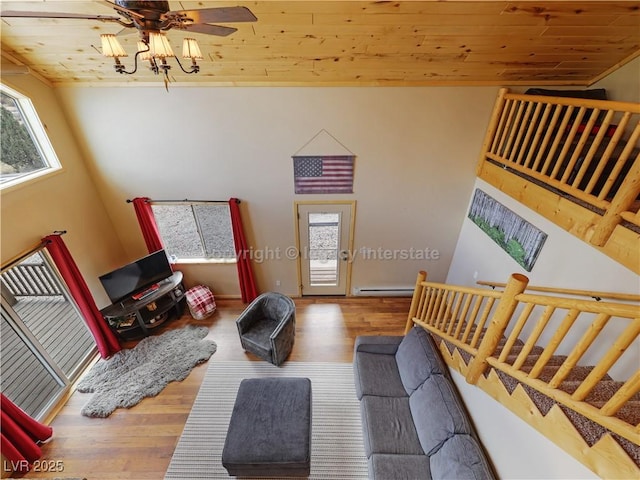 living room with stairs, wood finished floors, baseboard heating, wooden ceiling, and a ceiling fan