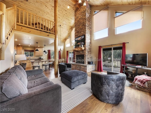 living room with light wood-type flooring, wood ceiling, a stone fireplace, and high vaulted ceiling