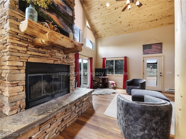 living room with wood ceiling, a stone fireplace, baseboard heating, wood finished floors, and high vaulted ceiling