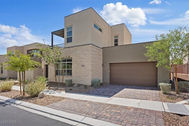 modern home with a garage, stucco siding, decorative driveway, and stone siding