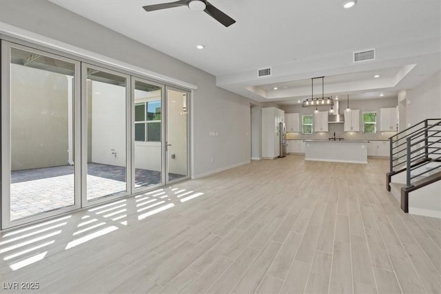 unfurnished living room with a tray ceiling, visible vents, and baseboards