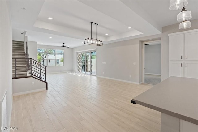 unfurnished living room featuring stairs, baseboards, a raised ceiling, and light wood-style floors