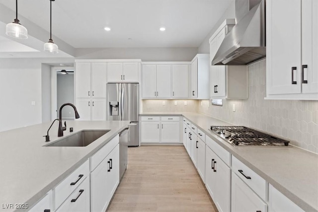 kitchen featuring pendant lighting, wall chimney range hood, white cabinets, a sink, and stainless steel appliances