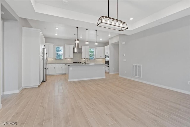 kitchen with visible vents, freestanding refrigerator, open floor plan, wall chimney range hood, and light wood-style flooring