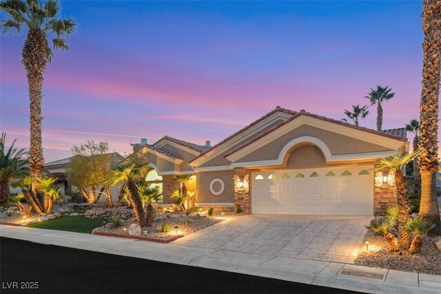 view of front of house with a garage, stucco siding, a tiled roof, and decorative driveway
