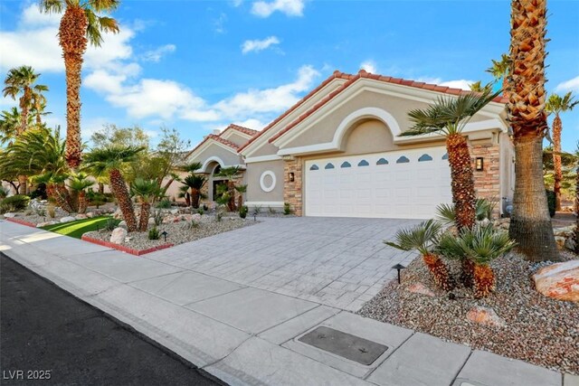 mediterranean / spanish home featuring decorative driveway, a garage, stucco siding, and a tiled roof