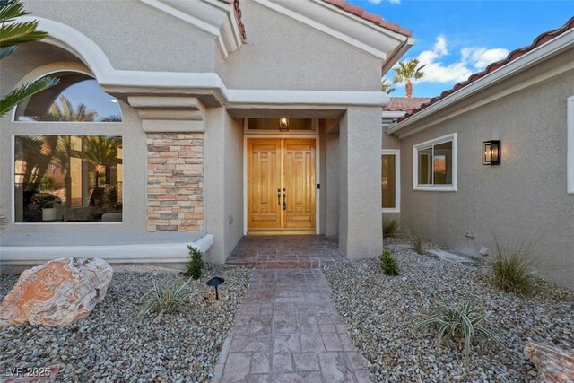 property entrance with stucco siding, a tiled roof, and stone siding
