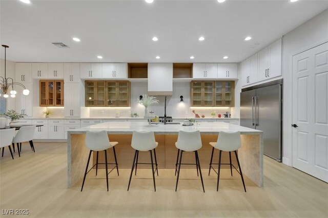 kitchen featuring white cabinets, light countertops, built in fridge, a large island, and light wood-type flooring