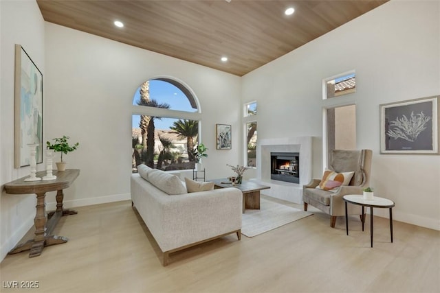 living area with baseboards, recessed lighting, a warm lit fireplace, and light wood-style flooring