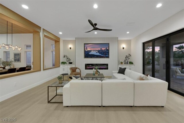 living area featuring recessed lighting, a large fireplace, wood finished floors, and ceiling fan with notable chandelier