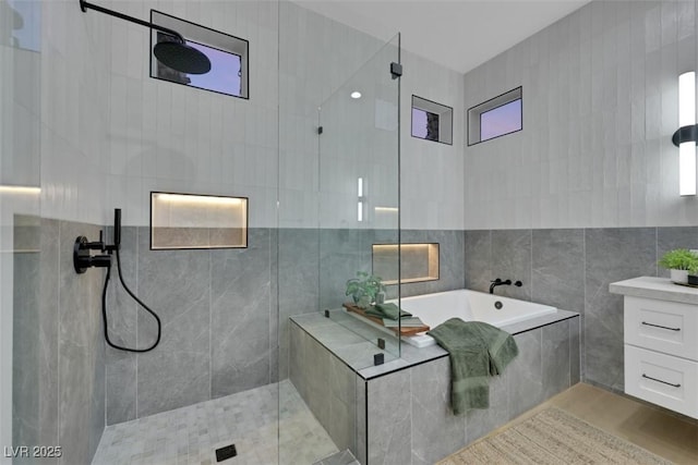 bathroom with a bath, tile walls, and tiled shower
