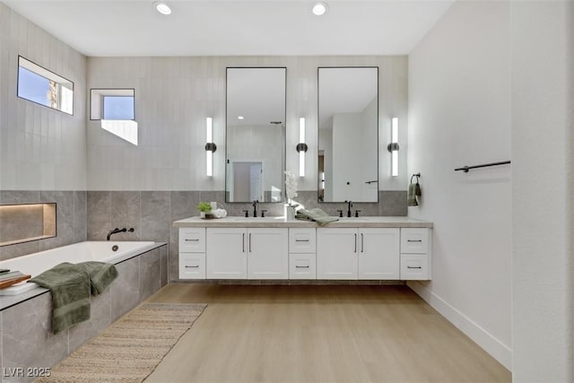 bathroom featuring double vanity, a sink, wood finished floors, and a bath