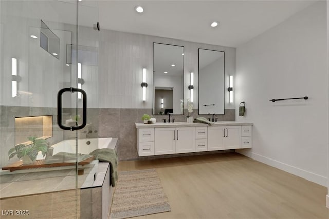 bathroom featuring a sink, double vanity, a shower stall, wood finished floors, and a garden tub