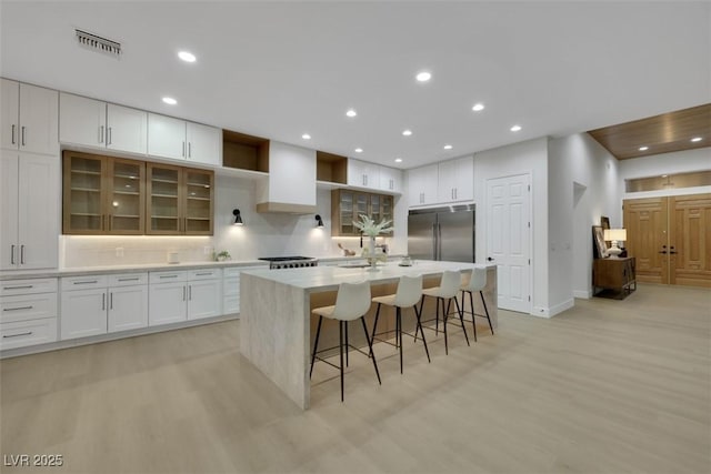 kitchen with stainless steel appliances, visible vents, light wood finished floors, and wall chimney exhaust hood