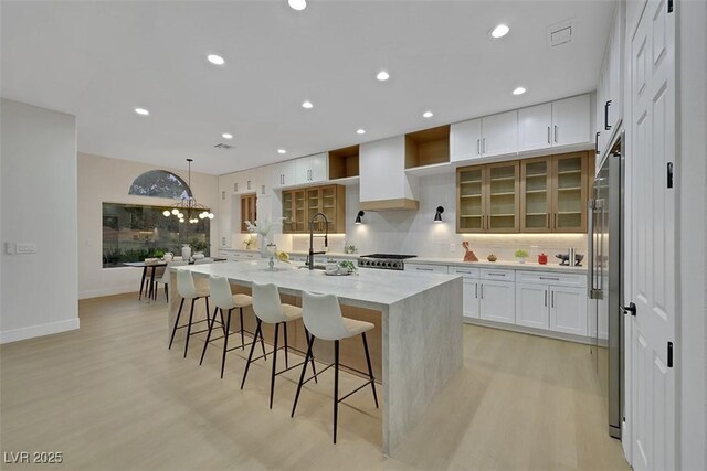 kitchen with tasteful backsplash, a sink, high end refrigerator, light wood finished floors, and white cabinetry