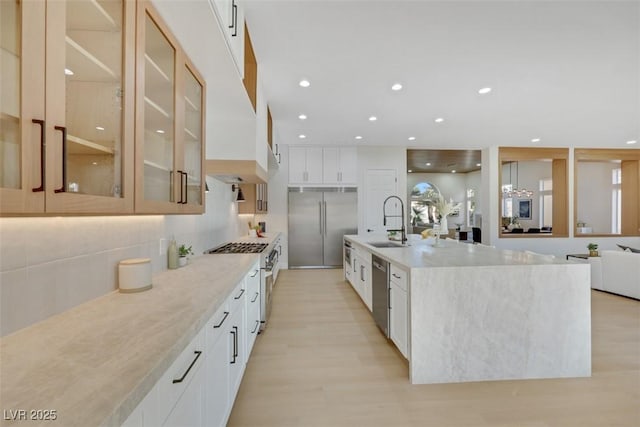 kitchen with decorative backsplash, high quality appliances, a sink, light wood finished floors, and glass insert cabinets