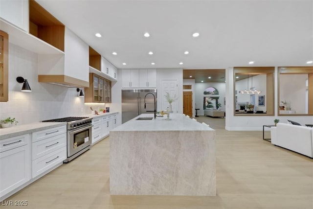 kitchen with high quality appliances, open shelves, open floor plan, white cabinetry, and an island with sink