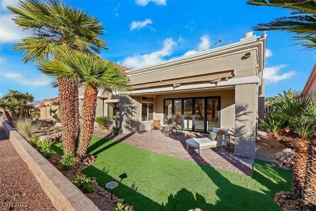 rear view of house with a lawn, a patio area, and stucco siding