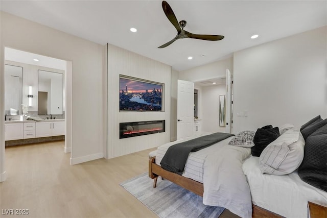 bedroom with recessed lighting, connected bathroom, light wood finished floors, and a glass covered fireplace