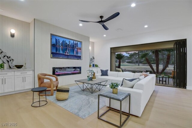 living area with recessed lighting, a ceiling fan, light wood-style flooring, and a glass covered fireplace