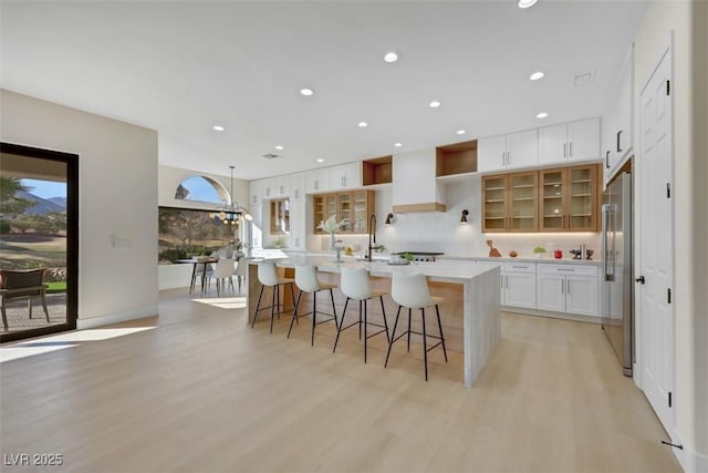 kitchen featuring a kitchen island with sink, tasteful backsplash, high end refrigerator, white cabinets, and light wood finished floors