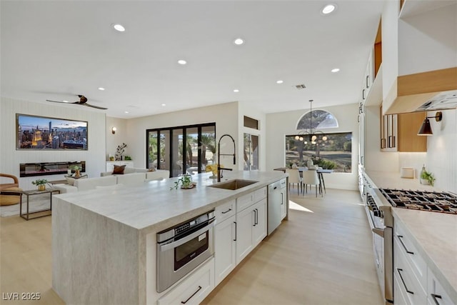 kitchen featuring a kitchen island with sink, stainless steel stove, a sink, light wood finished floors, and dishwasher