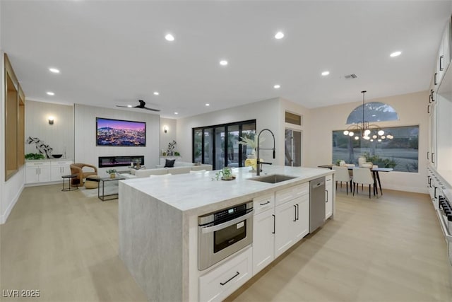 kitchen with a sink, stainless steel dishwasher, a center island with sink, and light wood finished floors