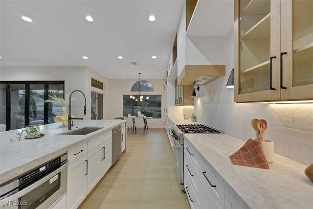 kitchen featuring backsplash, custom range hood, a sink, glass insert cabinets, and stainless steel appliances