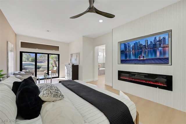 bedroom featuring a glass covered fireplace, wood finished floors, baseboards, connected bathroom, and a ceiling fan