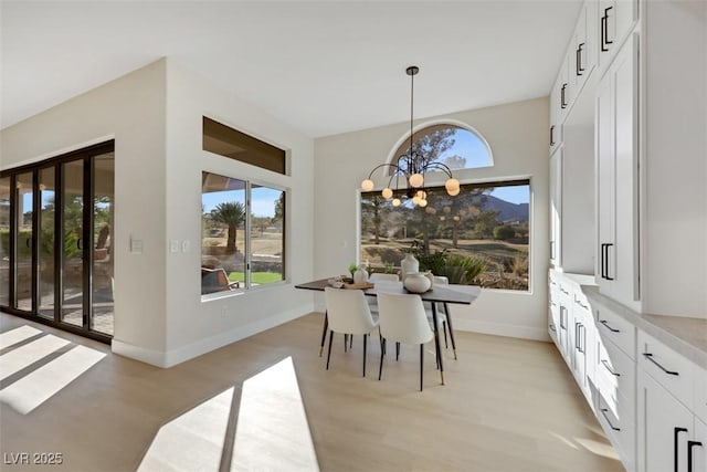 dining area with light wood-type flooring, baseboards, and a chandelier