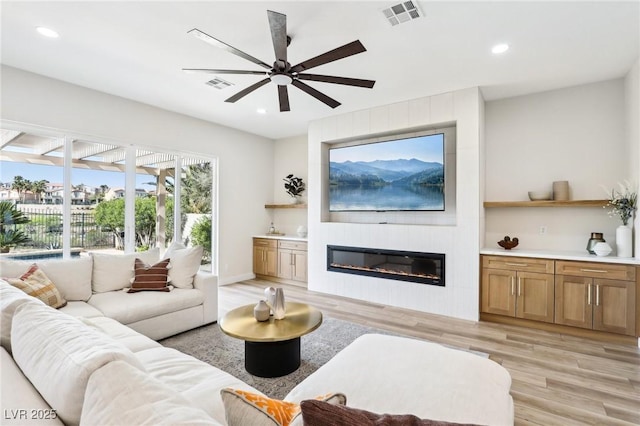living room with a ceiling fan, visible vents, a fireplace, light wood-type flooring, and recessed lighting