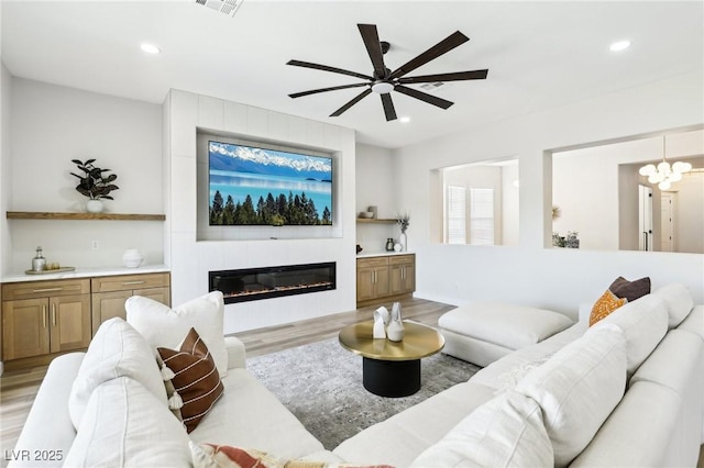 living room featuring recessed lighting, ceiling fan, a large fireplace, and light wood-style flooring