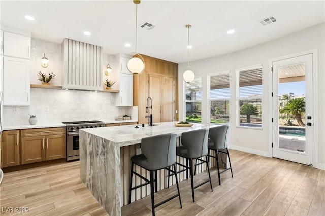 kitchen featuring stainless steel stove, a sink, ventilation hood, and visible vents