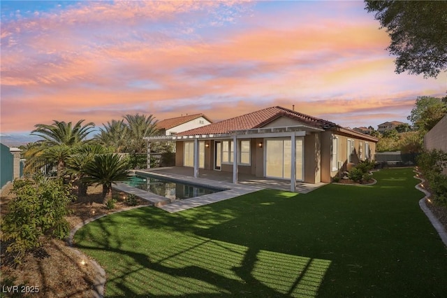 back of house with a tiled roof, a lawn, an outdoor pool, a patio, and stucco siding
