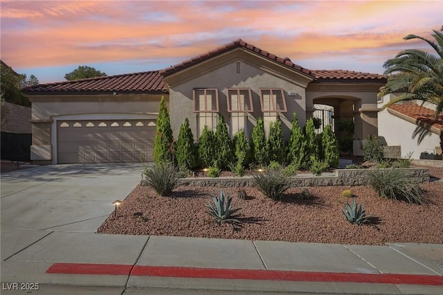 mediterranean / spanish-style house with a tiled roof, stucco siding, concrete driveway, and a garage