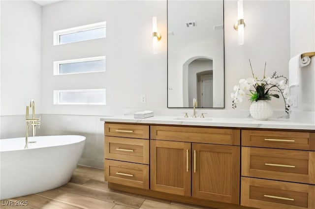 full bathroom featuring vanity, a freestanding bath, visible vents, and wood finished floors