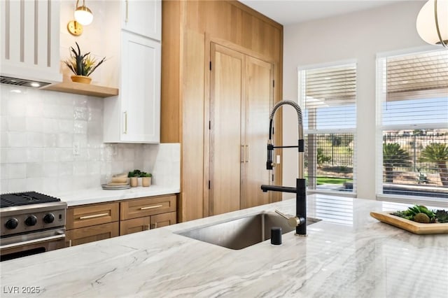kitchen featuring backsplash, a sink, stainless steel stove, and light stone counters