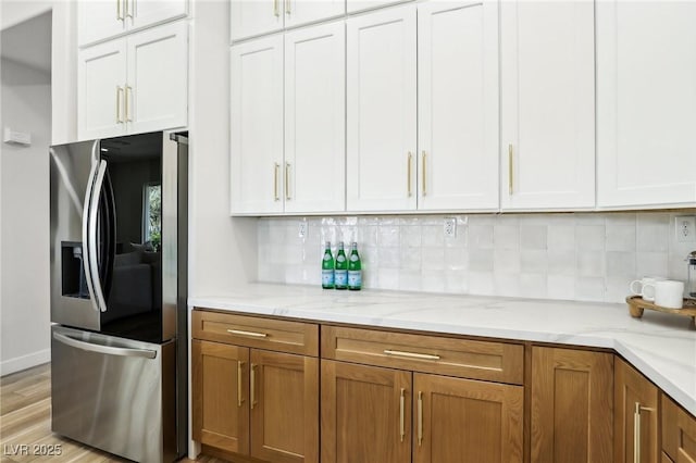 kitchen with brown cabinetry, stainless steel refrigerator with ice dispenser, tasteful backsplash, light stone counters, and light wood-style flooring