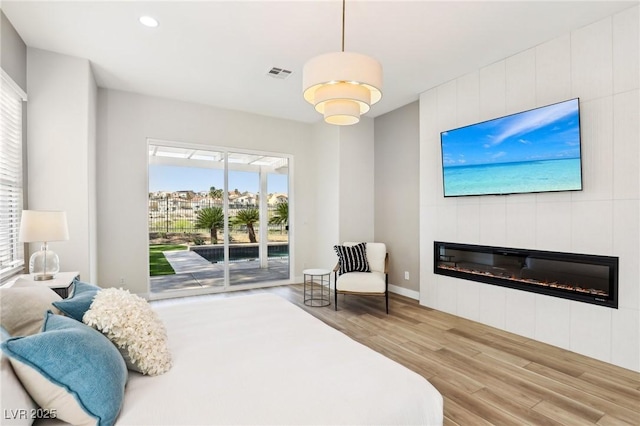 bedroom featuring a large fireplace, access to exterior, recessed lighting, wood finished floors, and visible vents
