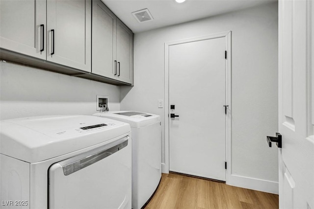 washroom with light wood-style floors, visible vents, cabinet space, and washing machine and clothes dryer