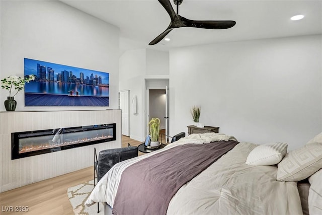 bedroom with a glass covered fireplace, a ceiling fan, recessed lighting, and wood finished floors