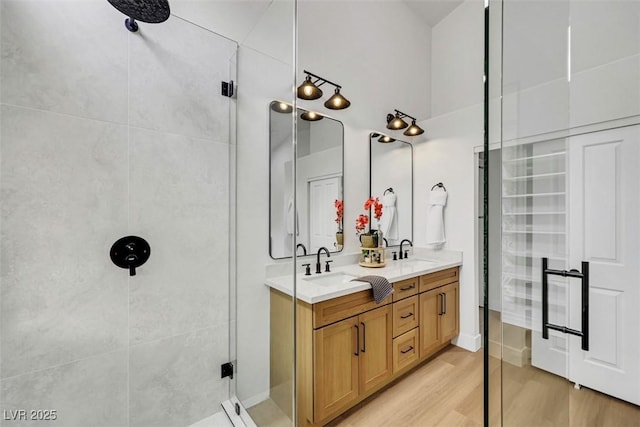 full bath featuring a sink, a shower stall, double vanity, and wood finished floors