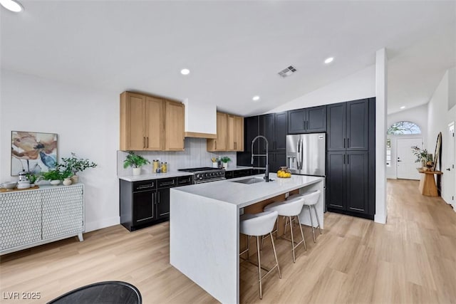 kitchen featuring appliances with stainless steel finishes, tasteful backsplash, light wood-type flooring, a sink, and light countertops