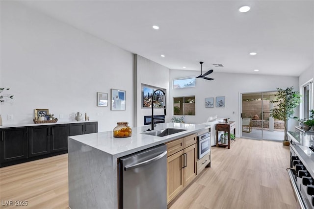 kitchen featuring ceiling fan, a sink, light wood finished floors, stainless steel dishwasher, and vaulted ceiling