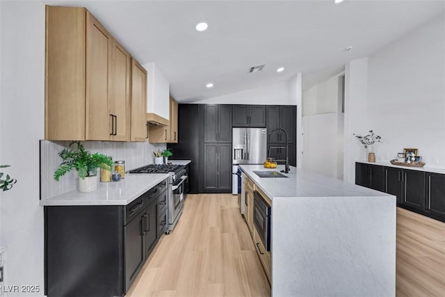 kitchen featuring visible vents, appliances with stainless steel finishes, a sink, light wood finished floors, and lofted ceiling