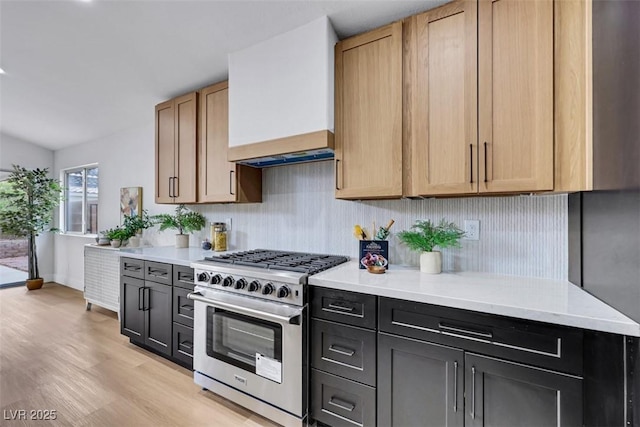 kitchen with high end stove, tasteful backsplash, baseboards, custom exhaust hood, and light wood finished floors