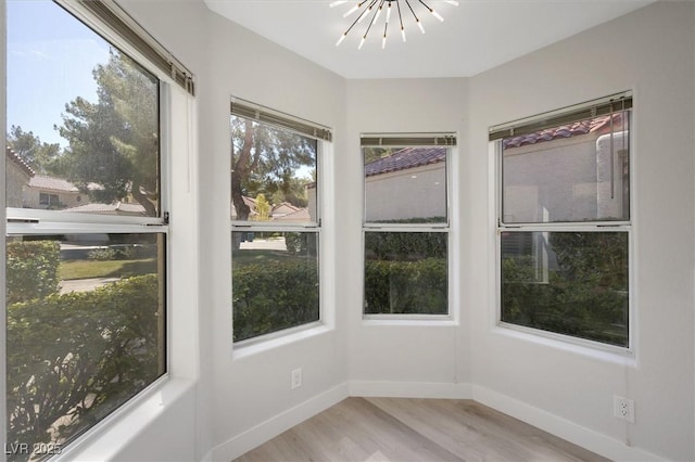 unfurnished sunroom with baseboards, wood finished floors, and a chandelier