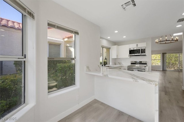 kitchen with visible vents, a sink, light wood finished floors, a notable chandelier, and stainless steel appliances