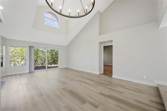 unfurnished living room featuring baseboards, light wood-style floors, high vaulted ceiling, and an inviting chandelier